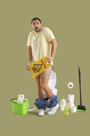 Shocked young man with caution sign and cleaning supplies near toilet bowl on green background