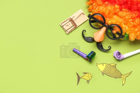 Clown wig with funny glasses, mousetrap and paper fishes on green background. April Fools Day