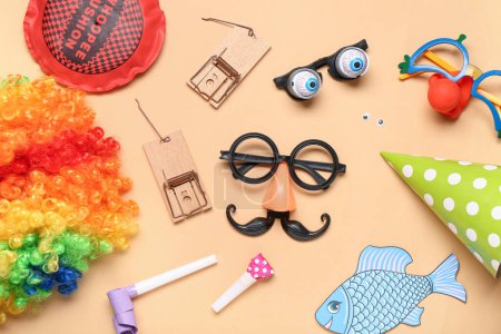 Funny glasses with clown wig, whoopee cushion and mousetraps on beige background. April Fool Day