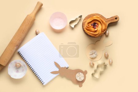 Téléchargez les photos : Bloc-notes vierge pour recettes avec pain sucré, décor de Pâques et outils de cuisson sur fond beige - en image libre de droit