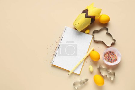 Téléchargez les photos : Bloc-notes vierge pour recettes avec stylo, oeufs de Pâques et outils de cuisson sur fond beige - en image libre de droit
