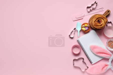 Téléchargez les photos : Bloc-notes vierge pour recettes avec pain sucré, décor de Pâques et outils de cuisson sur fond rose - en image libre de droit