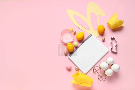 Téléchargez les photos : Bloc-notes vierge pour recettes avec oreilles de lapin, oeufs de Pâques et moules à pâtisserie sur fond rose - en image libre de droit