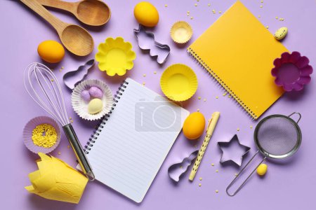Téléchargez les photos : Carnets vierges pour recettes avec stylo, oeufs de Pâques et outils de cuisson sur fond lilas - en image libre de droit