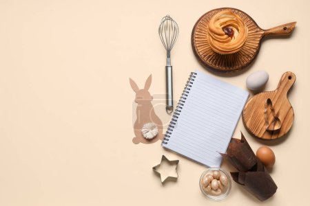 Téléchargez les photos : Bloc-notes vierge pour recettes avec pain sucré, décor de Pâques et outils de cuisine sur fond beige - en image libre de droit