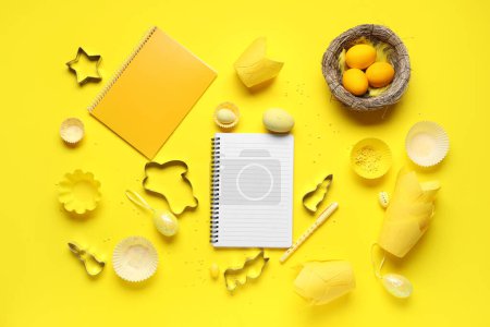 Téléchargez les photos : Bloc-notes vierges pour recettes avec stylo, oeufs de Pâques et outils de cuisson sur fond jaune - en image libre de droit