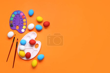 Foto de Paletas de pintura, huevos de Pascua y pinceles sobre fondo de color. Concepto Pascua. - Imagen libre de derechos