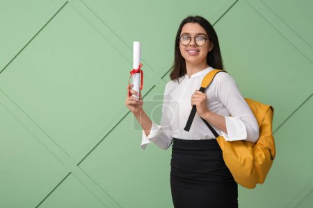 Photo for Happy smiling female student with diploma and backpack on green wooden background - Royalty Free Image