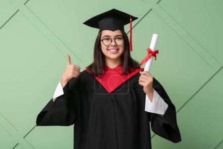 Photo for Happy female graduating student with diploma showing thumb-up on green wooden background - Royalty Free Image
