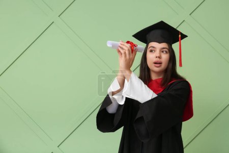 Photo for Female graduating student with diploma on green wooden background - Royalty Free Image