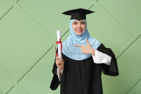 Photo for Happy Muslim female graduating student pointing at diploma on green wooden background - Royalty Free Image