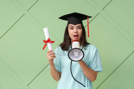 Photo for Surprised female medical student in graduation hat with diploma and megaphone on green wooden background - Royalty Free Image