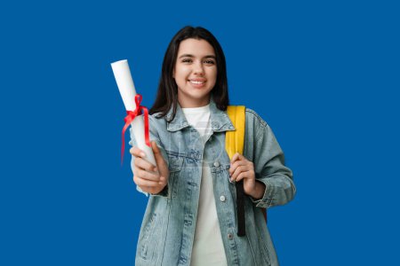 Photo for Happy smiling female student with backpack and diploma on blue background - Royalty Free Image