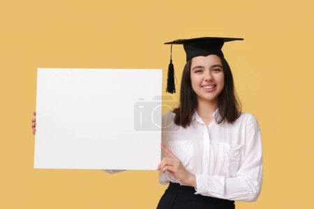 Photo for Happy smiling female student in graduation hat with blank poster on yellow background - Royalty Free Image
