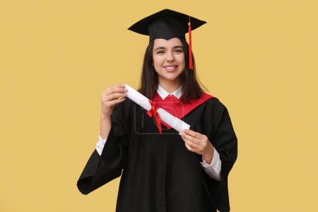 Photo for Happy female graduating student with diploma on yellow background - Royalty Free Image