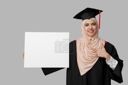 Photo for Happy Muslim female graduating student pointing at blank poster on white background - Royalty Free Image