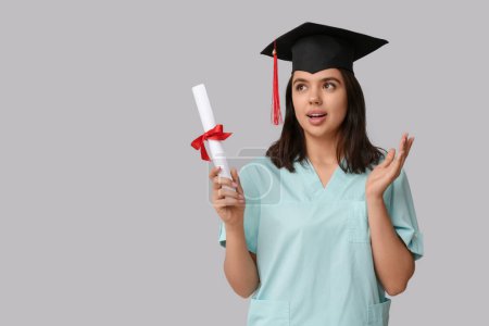 Photo for Surprised female medical student in graduation hat with diploma on white background - Royalty Free Image