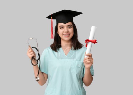 Photo for Happy female medical student in graduation hat with stethoscope and diploma on white background - Royalty Free Image
