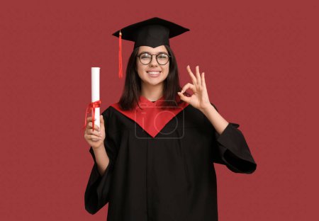 Photo for Happy female graduating student with diploma showing OK gesture on red background - Royalty Free Image