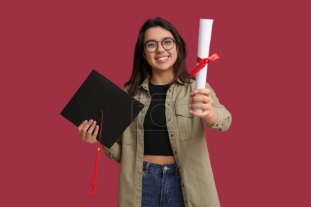Photo for Happy smiling female student with graduation hat and diploma on red background - Royalty Free Image