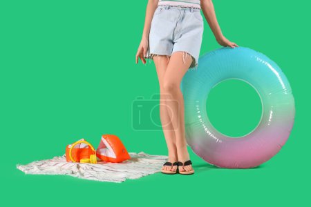 Jeune femme avec anneau gonflable, serviette et écouteurs sur fond vert. Concept vacances d'été