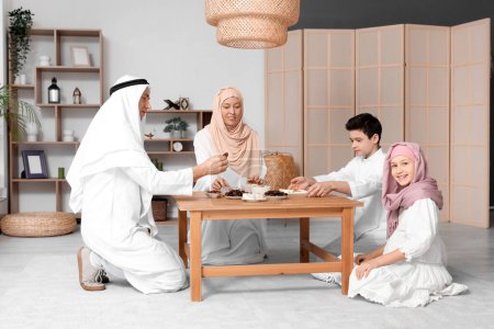 Glückliche muslimische Familie am Tisch mit traditionellen Süßigkeiten im Wohnzimmer. Eid al-Fitr-Feier