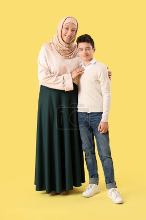 Happy Muslim mother and her son on yellow background. Eid al-Fitr celebration