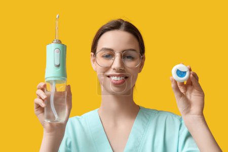 Dentiste féminine avec irrigateur oral et fil dentaire sur fond jaune