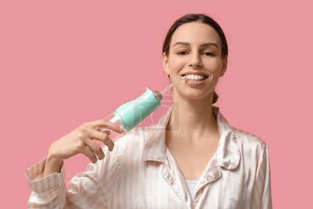 Schöne junge Frau mit oralem Bewässerungsgerät auf rosa Hintergrund