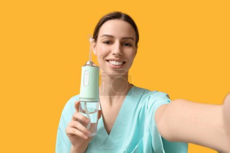 Female dentist with oral irrigator on yellow background