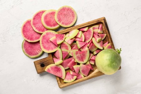 Wooden board with pieces of ripe watermelon radishes on white background