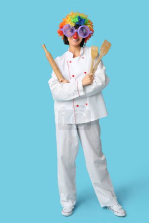 Foto de Divertido joven chef con utensilios de cocina sobre fondo azul. Día del Loco - Imagen libre de derechos