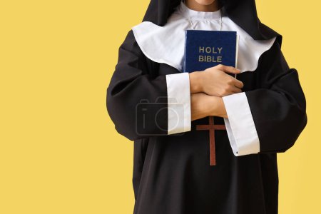 Joven monja con Biblia sobre fondo amarillo