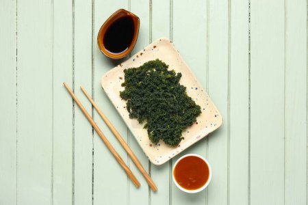Teller mit gesunden Algen, Essstäbchen und Soßen auf farbigem Holzhintergrund