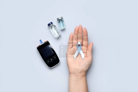 Woman with awareness ribbon, glucometer and insulin on light background. Diabetes concept