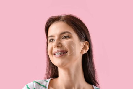Young woman with dental braces on pink background, closeup