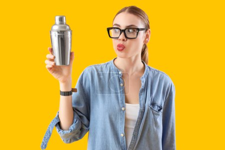 Thoughtful female bartender with shaker on yellow background