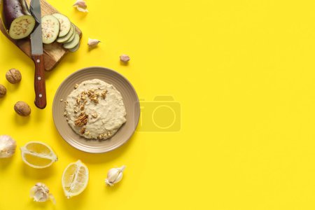 Plate of tasty baba ghanoush with ingredients on yellow background