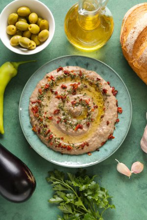 Plate of tasty baba ghanoush with ingredients on green background