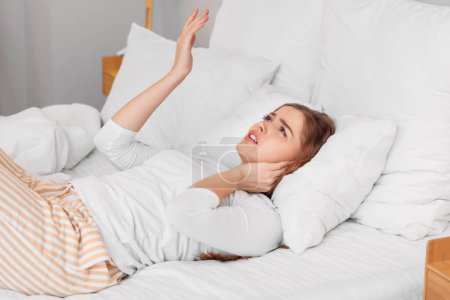 Junge Frau mit Kopfkissen leidet unter lauten Nachbarn im Schlafzimmer