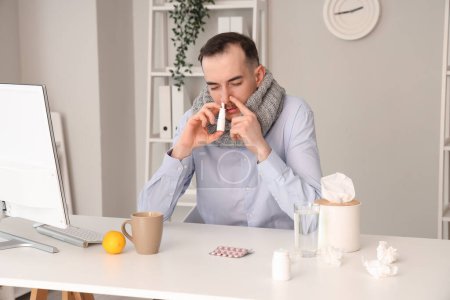 Téléchargez les photos : Homme d'affaires malade avec écharpe en utilisant des gouttes nasales au bureau - en image libre de droit