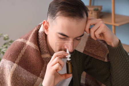 Téléchargez les photos : Jeune homme malade à carreaux utilisant des gouttes nasales à la maison, gros plan - en image libre de droit