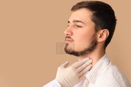 Endocrinologist examining thyroid gland of young man on beige background