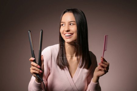 Schöne junge Frau mit Haarglätter und Kamm auf rosa Hintergrund