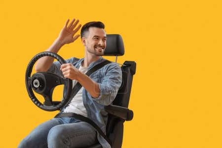 Schöner Mann mit Lenkrad wedelt mit der Hand im Autositz auf gelbem Hintergrund