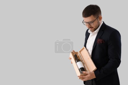 Photo for Young sommelier holding box with bottle of red wine on grey background - Royalty Free Image