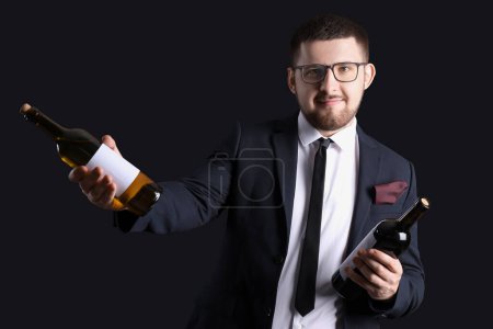 Photo for Young sommelier holding bottles with different types of wine on black background - Royalty Free Image