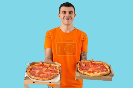 Junger Mann mit leckerer Pfefferoni-Pizza auf blauem Hintergrund