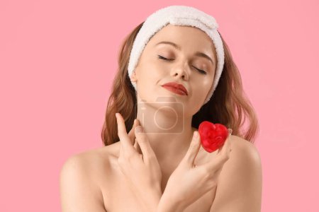 Beautiful young woman in bath headband with heart-shaped soap on pink background, closeup