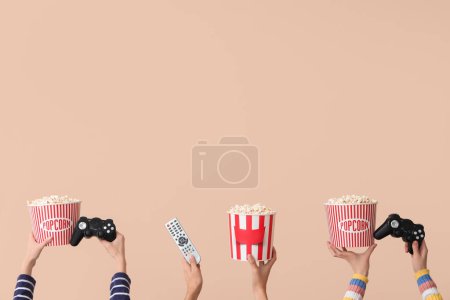 Photo for Many hands with buckets of popcorn, TV remote and game pads on beige background - Royalty Free Image